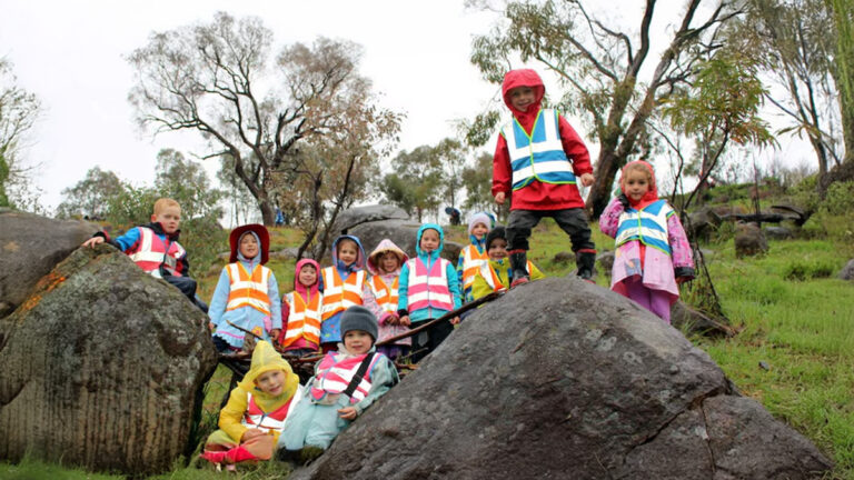 Chapman Primary Kindergarten children wearing safety vests while exploring nature and climbing rocks at nearby Cooleman Ridge in Canberra.