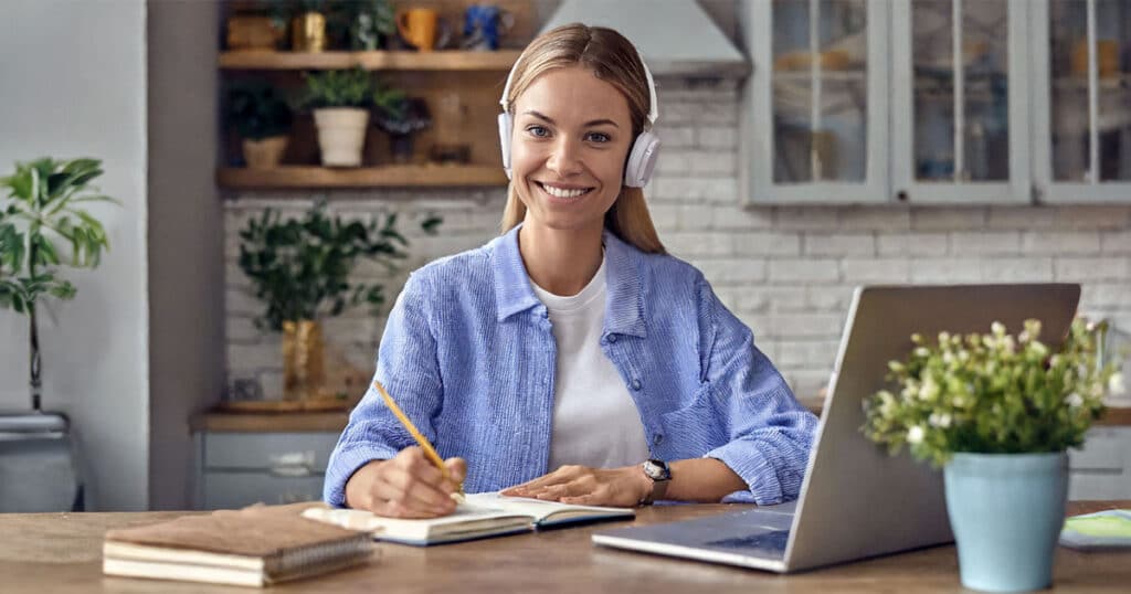 Smiling woman taking notes from laptop at kitchen table